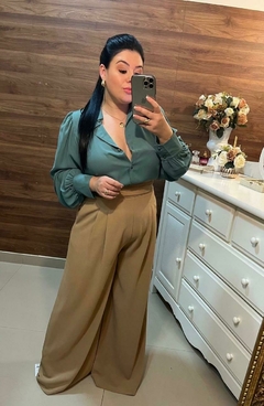 Mulher posando para uma selfie em um espelho, vestindo uma blusa verde e calças largas bege. Pantalona nude, pantalona cor nude, pantalona, calça pantalona, calça nude, calça clara