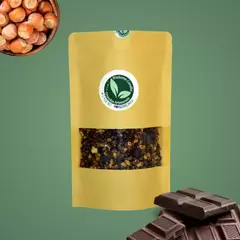 Pacote de granola artesanal de cacau e avelã, com avelãs e pedaços de chocolate ao fundo.