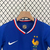 Uniforme infantil da seleção francesa, composto por camiseta azul e shorts brancos, com detalhes em vermelho e o logo da Nike.