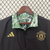 Agasalho corta vento da Adidas, modelo Manchester United, com design dupla face nas cores preta e verde, apresentando o logotipo do clube e detalhes em dourado.