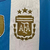 Camisa de futebol masculina da seleção argentina, modelo 2024/25, nas cores azul e branca, com detalhes em dourado.