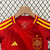 Uniforme infantil da seleção da Espanha, composto por camiseta vermelha com detalhes amarelos e calção azul, da marca Adidas.