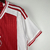 Camisa masculina do Ajax para a temporada 2023/2024, predominantemente branca e vermelha, com logo da Adidas e patrocinador Ziggo.