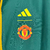 Agasalho corta vento da Manchester United, modelo 2023/24, nas cores verde e azul, com detalhes em amarelo e logo da Adidas.