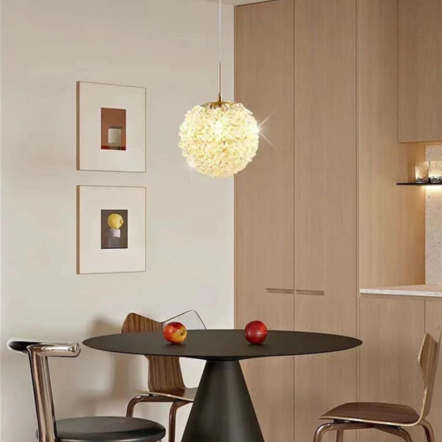 Luminária pendente em formato esférico com textura branca, iluminando uma mesa preta rodeada por cadeiras modernas em um ambiente de cozinha minimalista.