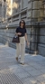 Mujer caminando por la calle con un polo de punto piqué en color azul y pantalones claros, sosteniendo un bolso de mano.