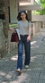 Mujer caminando con un jean clásico recto, camiseta gris y bolso burdeos en una calle iluminada por el sol.