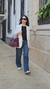 Mujer caminando por la calle con un blazer blanco, camiseta negra y jeans clásicos rectos, llevando un bolso burdeos.