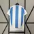 Camisa da Seleção da Argentina 24/25, azul e branca, com detalhes em dourado, incluindo patches de campeão e logotipo da Adidas.

