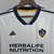 Camisa branca da LA Galaxy, modelo feminino, com logo da equipe e estampa da Herbalife Nutrition.

