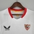 Camisa branca do Sevilla FC 22/23, modelo torcedor Castore, com detalhes em vermelho e patrocinadores visíveis.

