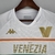 Camisa branca do Venezia FC com listras verdes, laranjas e detalhes em dourado, modelo Away 22/23 da Kappa para torcedores masculinos.

