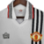 Camisa retrô branca do Manchester United, modelo de 1975/1980, com detalhes em preto e vermelho, incluindo o logo da equipe e a marca Admiral.

