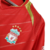 Camisa retrô do Liverpool da temporada 2005/2006, na cor vermelha, com detalhes em dourado e logotipo da Reebok.

