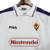 Camisa retrô branca da Fiorentina, modelo de 1998, com detalhes em azul e logo da Fila e Nintendo.

