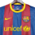 Camisa retrô do Barcelona 2010/2011 nas cores azul e grená, com detalhes em amarelo e o logo da Nike.

