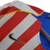 Camisa retrô do Atlético de Madrid da temporada 2004/2005, nas cores vermelha e branca, com detalhes em azul e logotipo da Nike.

