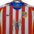 Camisa retrô do Atlético de Madrid da temporada 2004/2005, nas cores vermelha e branca, com detalhes em azul e logotipo da Nike.

