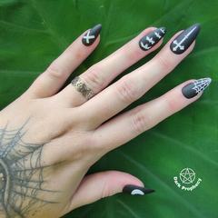 Anel Wicca de aço inoxidável exibido em uma mão com unhas decoradas em preto e desenhos temáticos.