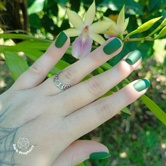 Anel Meia Lua em aço inoxidável exibido em uma mão com unhas verdes, em frente a uma flor.