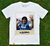 Camiseta branca com estampa de polaroide de Diego Maradona, sorrindo e levantando os braços em celebração, vestindo a camisa do Napoli.