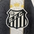 Detalhe do escudo do Santos Futebol Clube em uma camisa branca e preta, com estrelas e uma coroa acima do escudo.