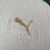 Logotipo dourado da Puma em uma camisa branca com detalhes verdes.