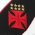 Emblema do Vasco da Gama com cruz vermelha e cinco estrelas douradas, destacando-se na camisa branca.