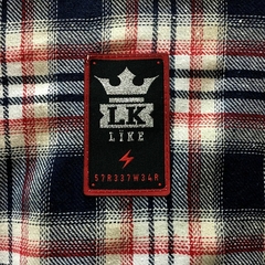 Close-up de uma camisa xadrez premium da marca LK-LIKE, com etiqueta preta destacando o logo e um símbolo de raio.