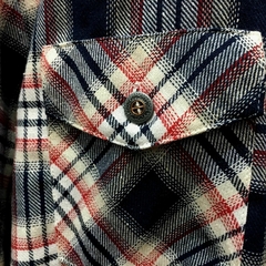 Detalhe de uma camisa xadrez premium da marca LK-LIKE, com estampa em vermelho, azul e branco, destacando o bolso e o botão.