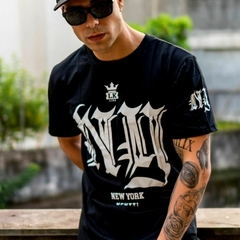 Homem usando camiseta preta da marca LK-LIKE com estampa "NY", posando em ambiente urbano.