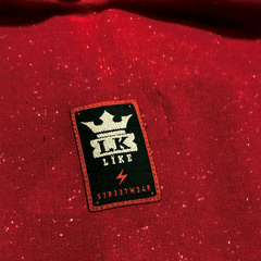 Imagem de um moletom premium vermelho da marca LK-LIKE, com um patch preto que exibe a inscrição "LK LIKE" e uma coroa acima do texto.