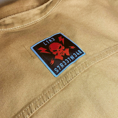 Imagem de um patch em uma jaqueta de sarja premium da marca LK-LIKE, apresentando uma caveira estilizada com letras e raios ao fundo.