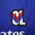 Emblema da camisa Lyon Away 23/24 da Adidas, apresentando as letras OL em fundo azul com detalhes em vermelho e azul.