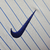 Logotipo da Nike em bordado azul sobre fundo branco listrado, parte da camisa da Seleção da França II 24/25 para torcedoras.