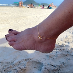 detalhe no tornozelo da tornozeleira semijoia corrente com pingentes estrela do mar, búzio e pérola banhado a ouro 18k