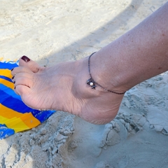 detalhe no tornozelo da tornozeleira semijoia corrente com pingentes estrela do mar, búzio e pérola banhado a ródio negro