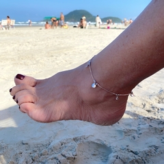 detalhe no tornozelo da tornozeleira semijoia com pingente moedas e ponto luz banhado a ródio
