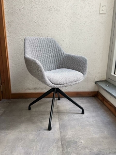 Un sillón giratorio tapizado en tela gris con diseño acolchado y base negra.