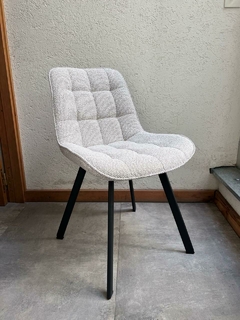 Silla tapizada en tela beige con diseño acolchado y patas negras