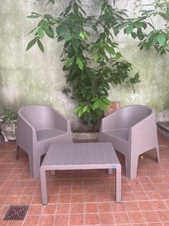 Conjunto de sillones de exterior color capuchino simulando ratán, con mesa en un ambiente natural rodeado de plantas.