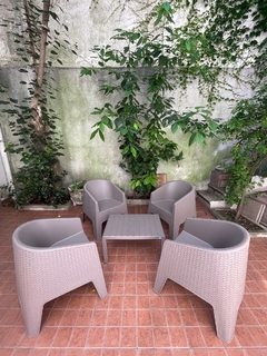 Conjunto de sillones de exterior color capuchino simulando ratán, con mesa en un ambiente natural rodeado de plantas.