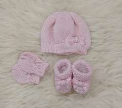 Conjunto de três peças em rosa, composto por um gorro, luvas e sapatinhos, todos de tricô.