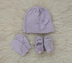 Conjunto de três peças para bebês, incluindo um gorro lilás, luvas e sapatinhos decorados com flores.