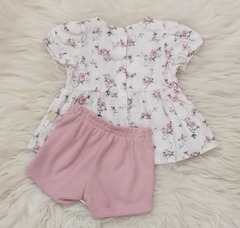 Conjunto de duas peças para crianças, incluindo uma blusa branca com estampa floral e um short rosa.