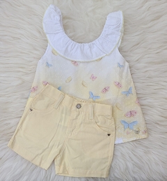 Conjunto Anjos composto por uma blusa branca com babado e estampas de borboletas coloridas, acompanhada de um short amarelo claro.