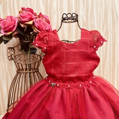 Vestido de festa infantil vermelho com detalhes em tule e pérolas, exposto em um cabideiro decorativo.