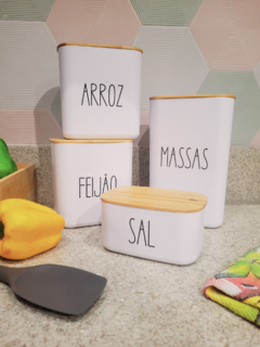 Potes herméticos brancos com tampas de bambu, etiquetados para arroz, feijão, massas e sal, dispostos em uma bancada de cozinha.