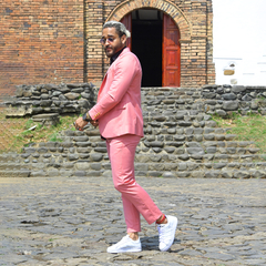 Hombre posando con un traje premium color rosado, complementado con zapatillas blancas, en un entorno al aire libre.