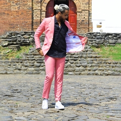 Hombre vistiendo un traje premium color rosado, con camisa negra y zapatillas blancas, mostrando el interior del saco, en un entorno al aire libre.